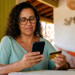 Pessoa consultando o pagamento do Bolsa Família em um celular ao lado de um cartão bancário, em ambiente doméstico