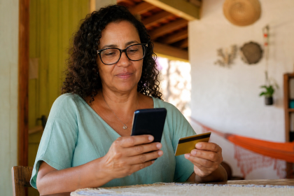 Pessoa consultando o pagamento do Bolsa Família em um celular ao lado de um cartão bancário, em ambiente doméstico