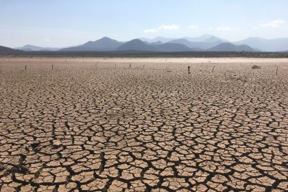 Paisagem rural extensa com o solo severamente rachado sob céu aberto, indicando condições de seca.