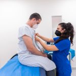 Profissional de enfermagem auxilia paciente durante um exame em ambiente hospitalar.