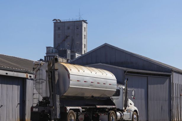 Caminhão semirreboque estacionado junto a um armazém industrial de grãos.