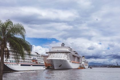 Navios de cruzeiro atracados em um porto tropical, com palmeiras ao redor e céu nublado.