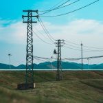 Linhas de transmissão de alta tensão próximas a aerogeradores em uma paisagem rural.